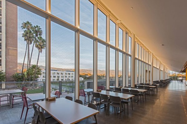 Empty tables in a dining commons near large windows that overlook an apartment complex, palm trees, and mountains