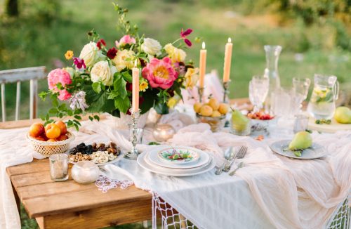 women's day, wedding, celebration, romance, picnic, nature concept - gorgeous table setting with snow white tablecloth, dishes, clear wine-glasses, silver candleholders and various fruits